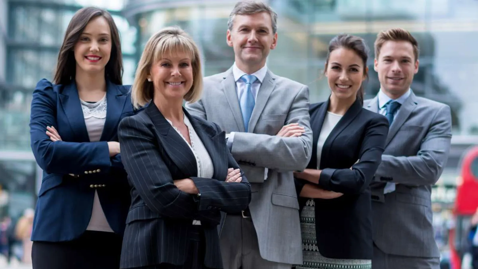 Confident diverse business team standing outdoors in formal attire with arms crossed in front of modern building.