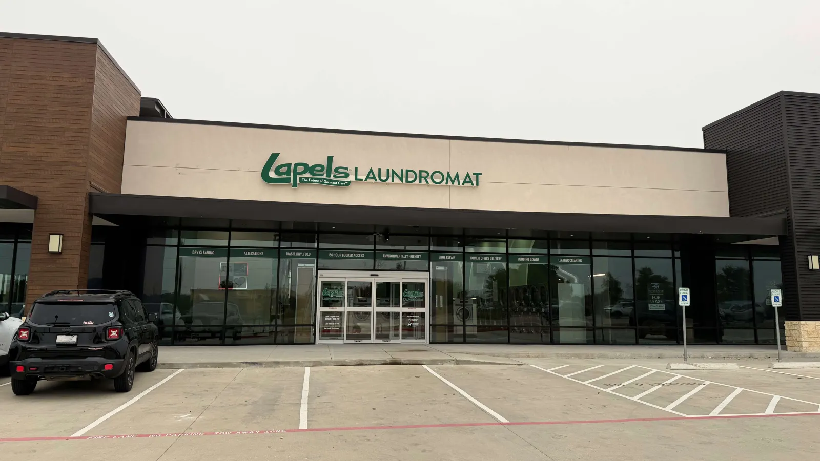 Exterior of Lapels Laundromat with glass storefront and parking lot on a cloudy day.