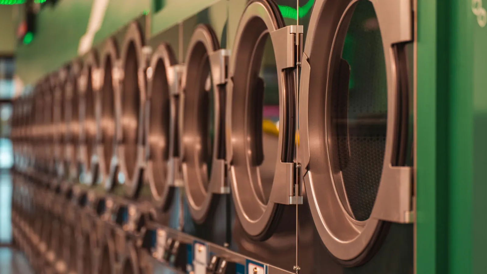 Row of modern front-loading washing machines with open doors in a laundromat