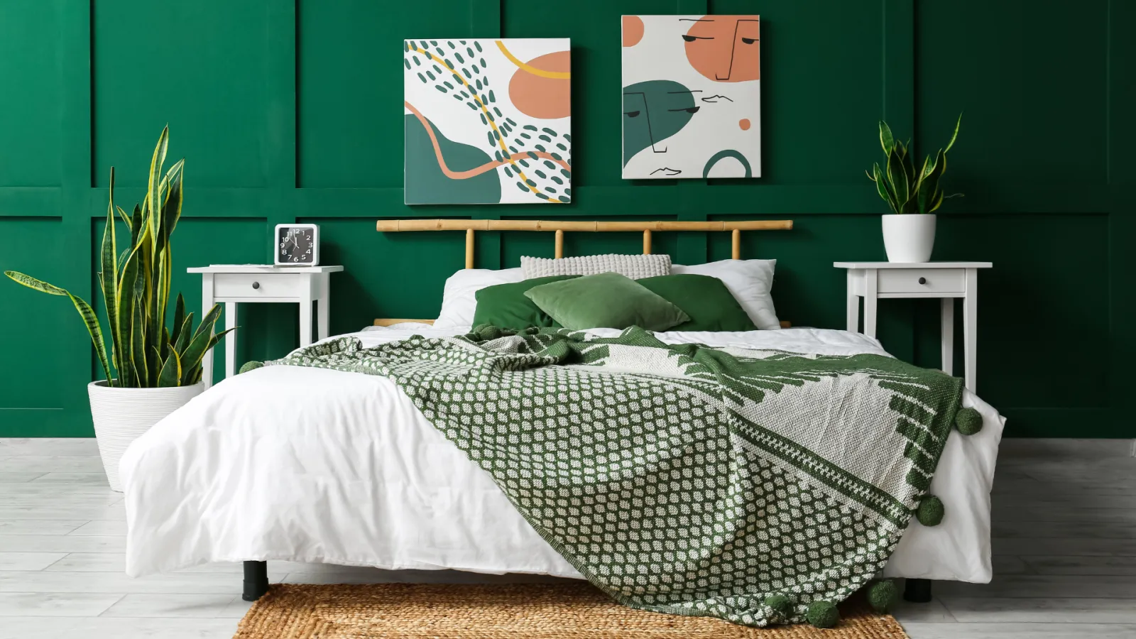Bedroom with green accent wall, white bed, green pillows, patterned blanket, plants, and abstract wall art.