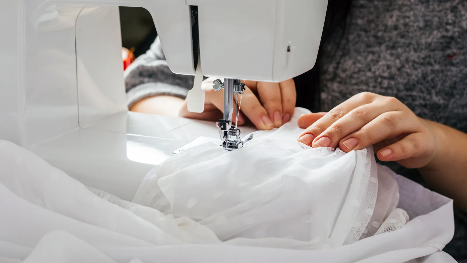 Close-up of hands sewing white fabric with polka dots on a sewing machine in natural light