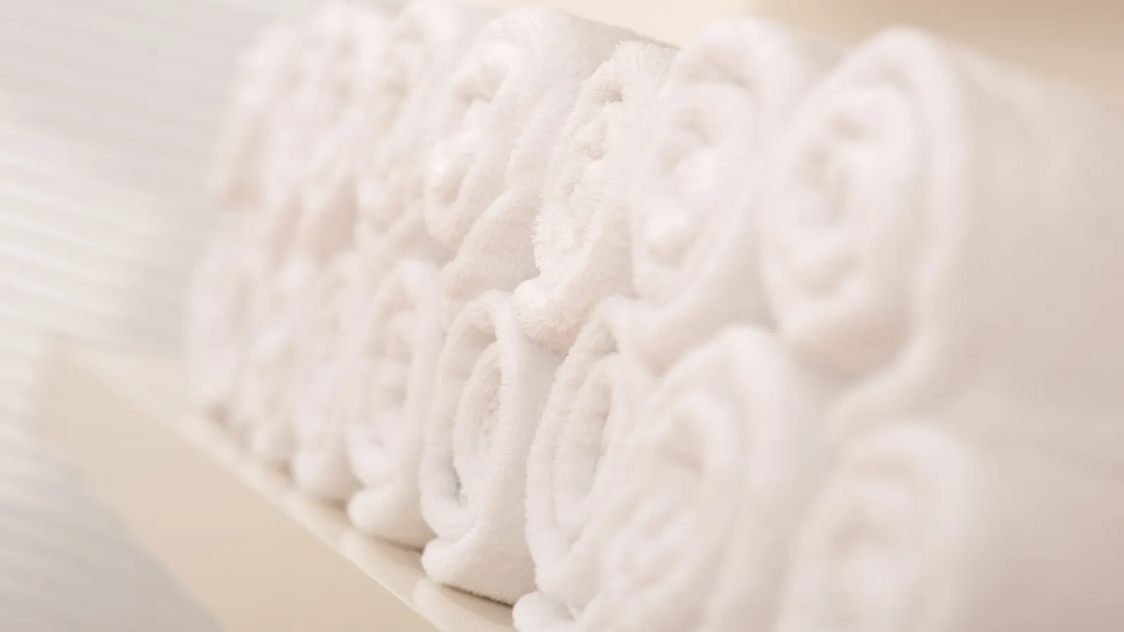 Stack of soft white towels neatly rolled and arranged on a wooden shelf in a bright space
