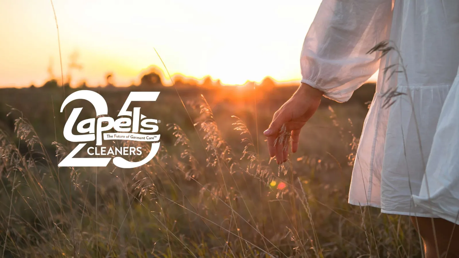 Person in white dress touching tall grass in a sunset field with Capels Cleaners 25th anniversary logo overlay.