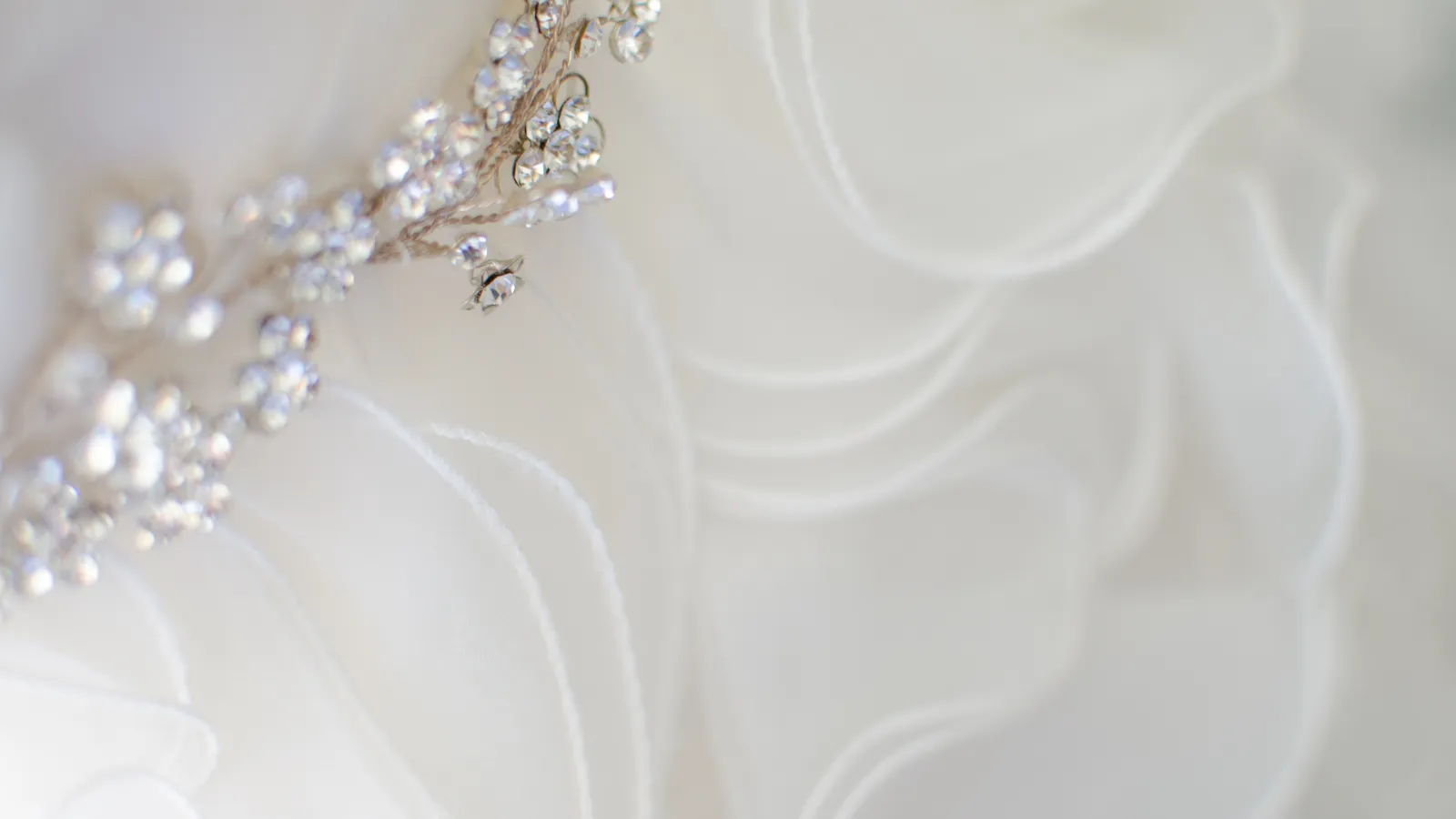 Close-up of a white wedding dress with delicate fabric ruffles and a sparkling crystal floral brooch.