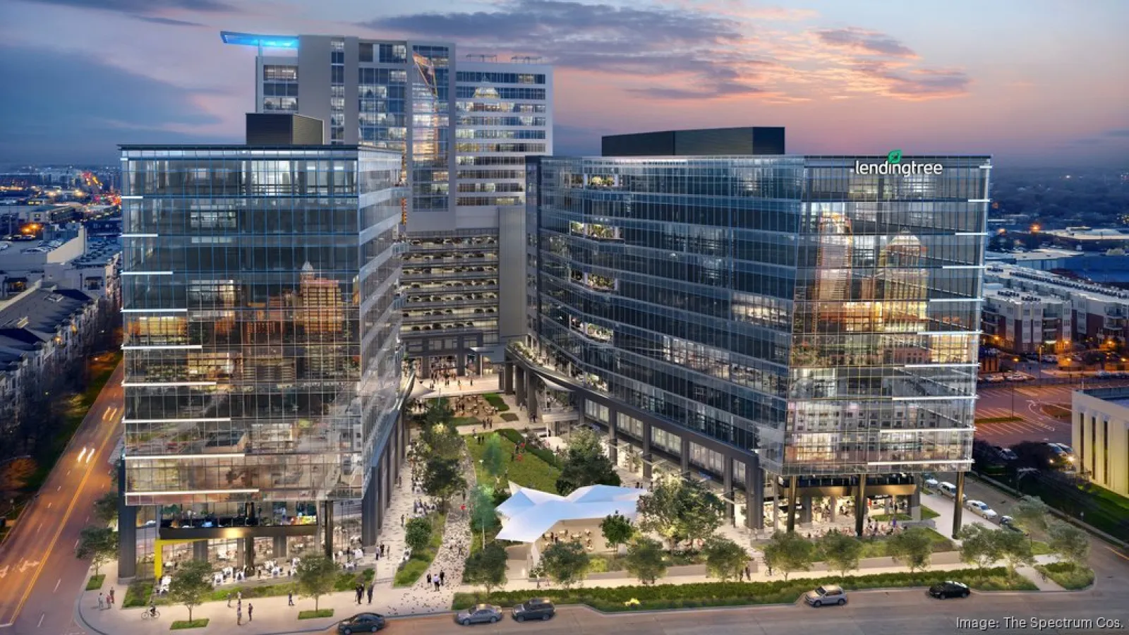 Modern office buildings with glass facades surrounding a green courtyard at twilight in an urban area.