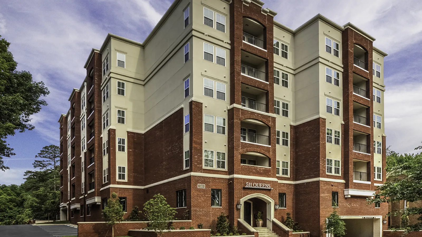 Modern five-story brick and beige apartment building with balconies under a partly cloudy sky.