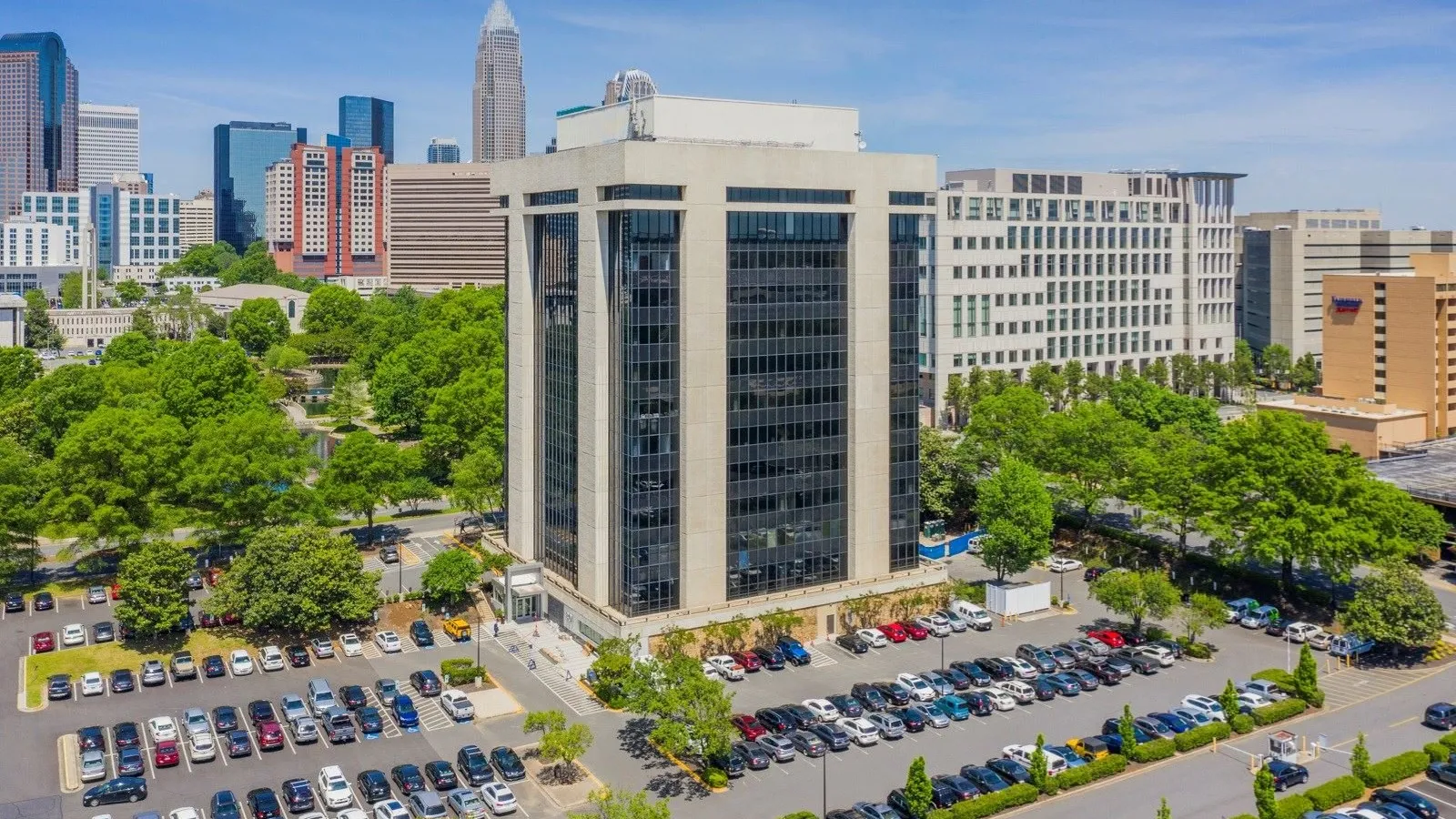 Aerial view of an office building with surrounding parking lots and a city skyline in the background on a clear day