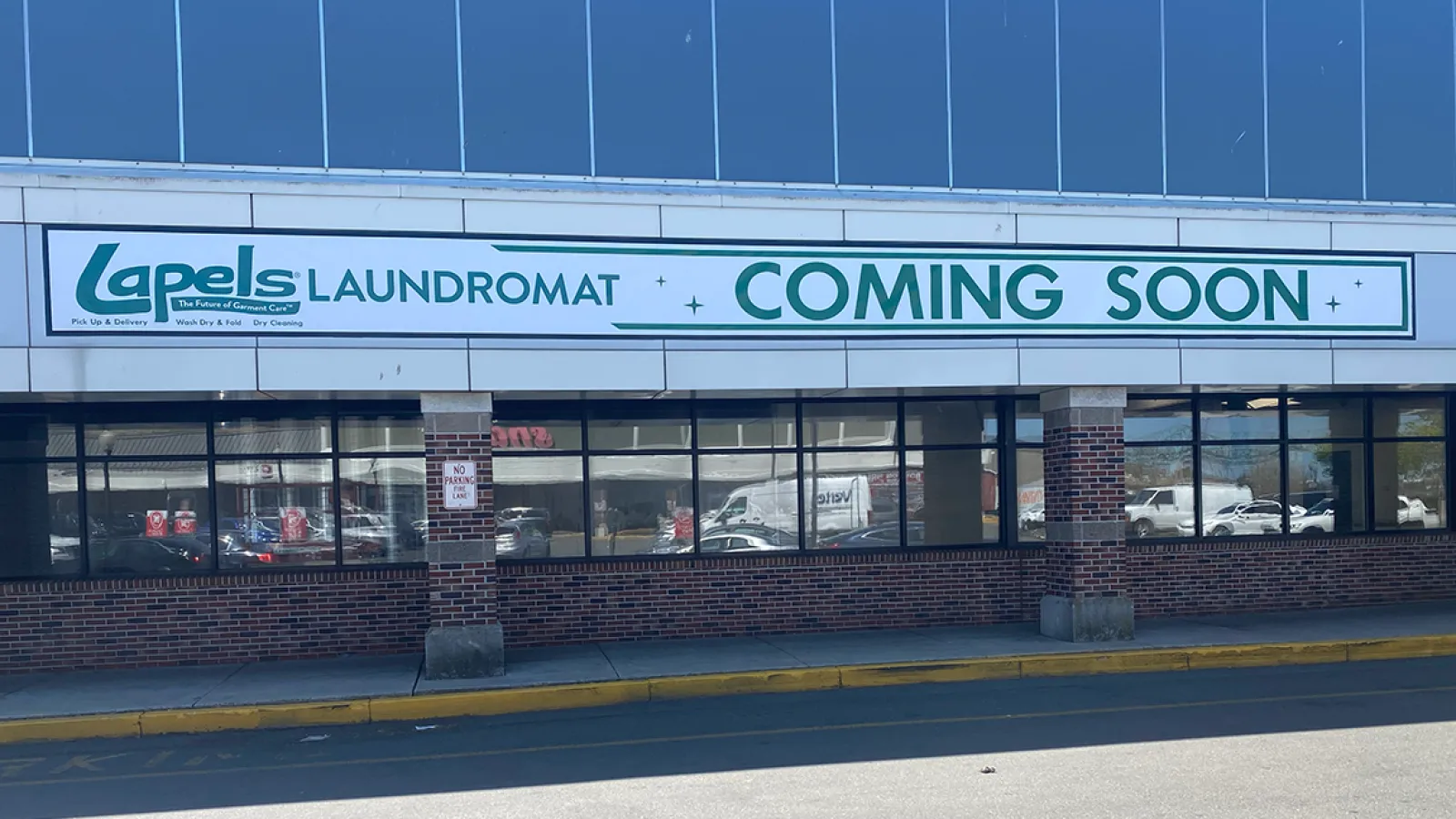 Lapels Laundromat storefront with large 'Coming Soon' sign in shopping center under blue sky