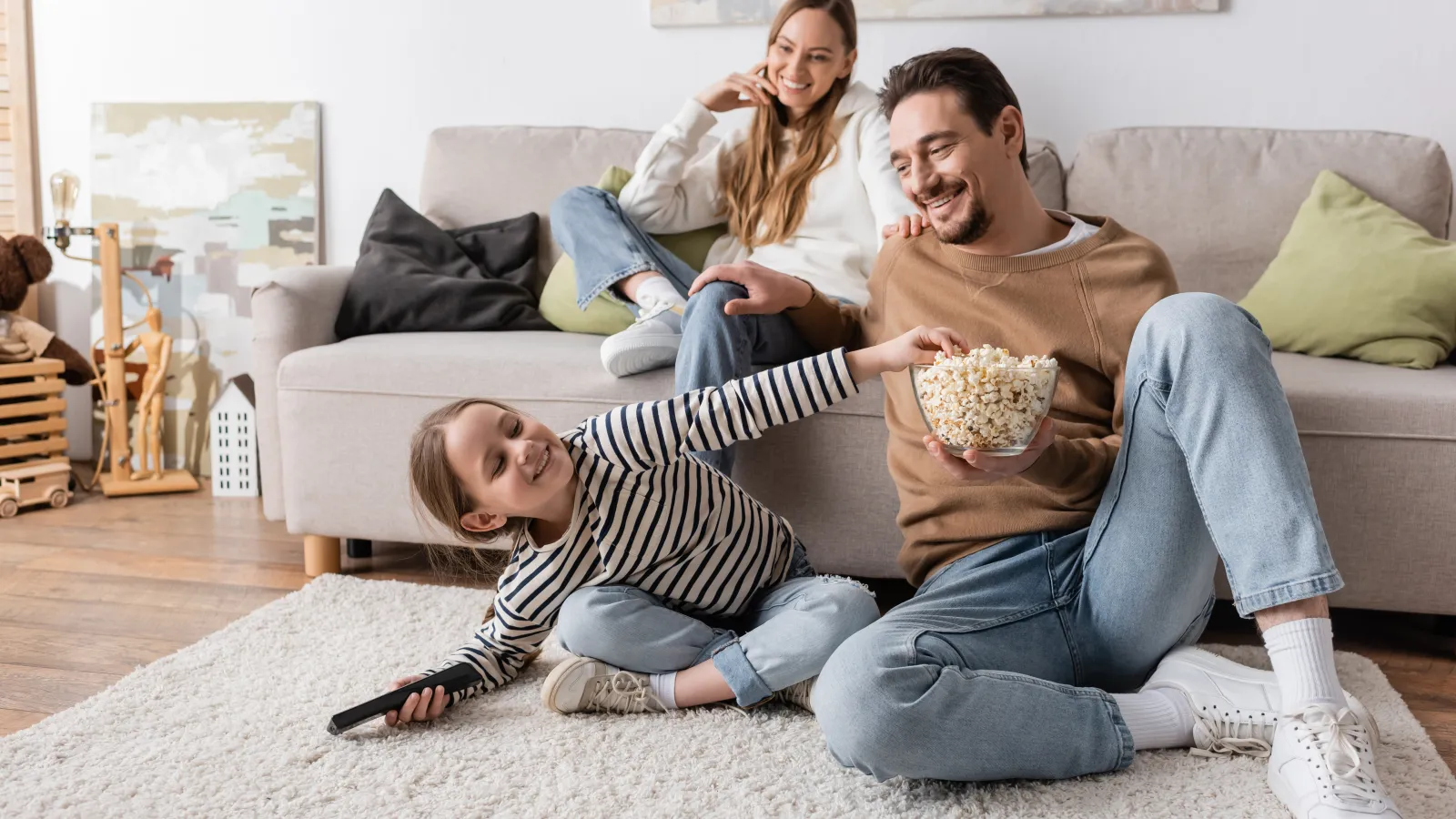 Happy family enjoying popcorn together in a cozy living room with casual outfits and relaxed atmosphere.