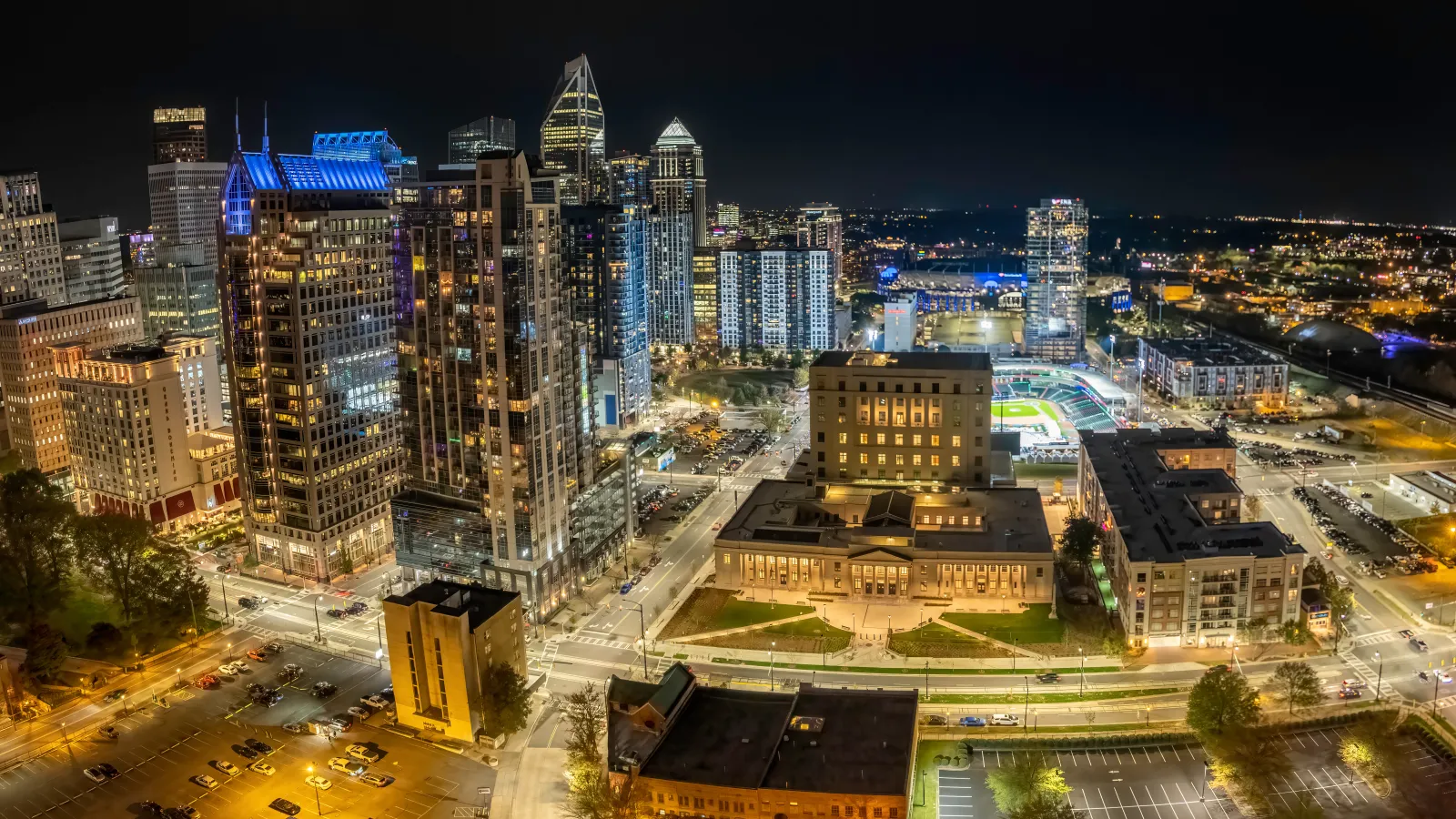 Nighttime aerial view of a vibrant cityscape with illuminated skyscrapers and busy streets.