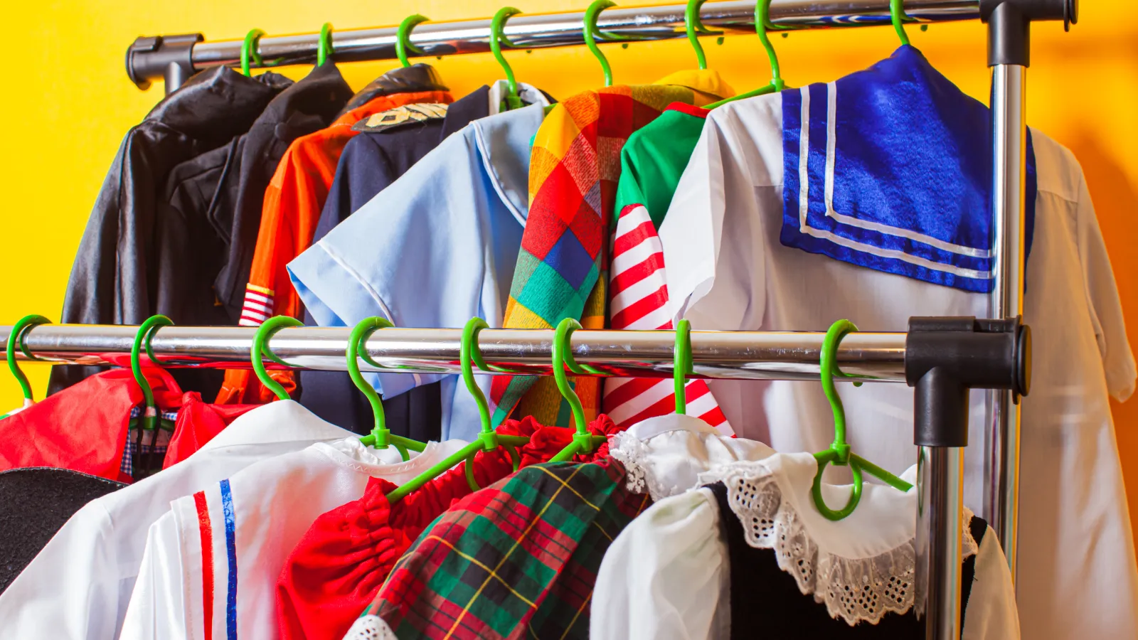 Colorful costumes including plaid, striped, and sailor outfits hanging on green hangers on a metal rack