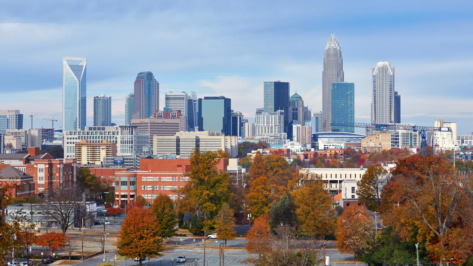 Charlotte skyline with modern skyscrapers and autumn foliage under a partly cloudy sky.