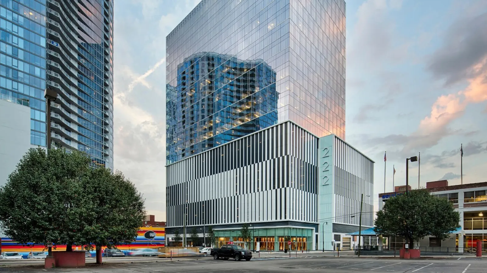 Modern glass office building with reflective windows and striped lower facade at sunset in urban setting