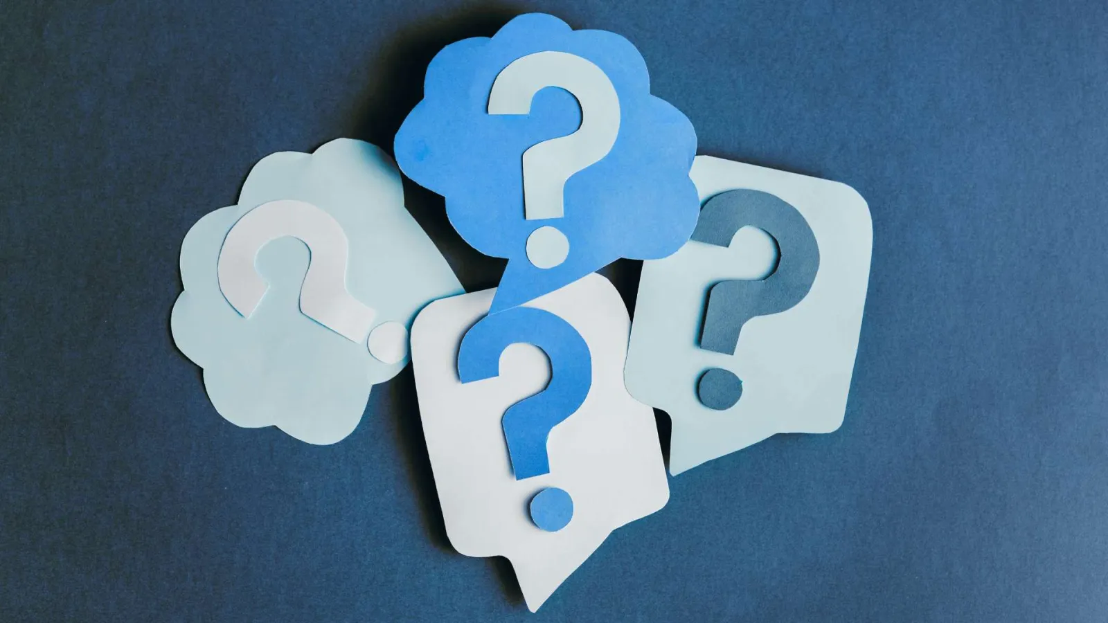 Blue and white paper speech bubbles with question marks on a dark blue background