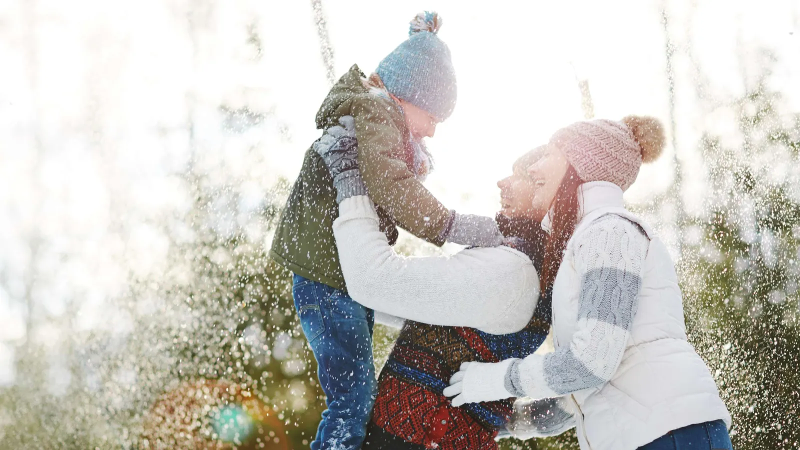 Happy family playing in the snow with winter clothes and joyful expressions outdoors.