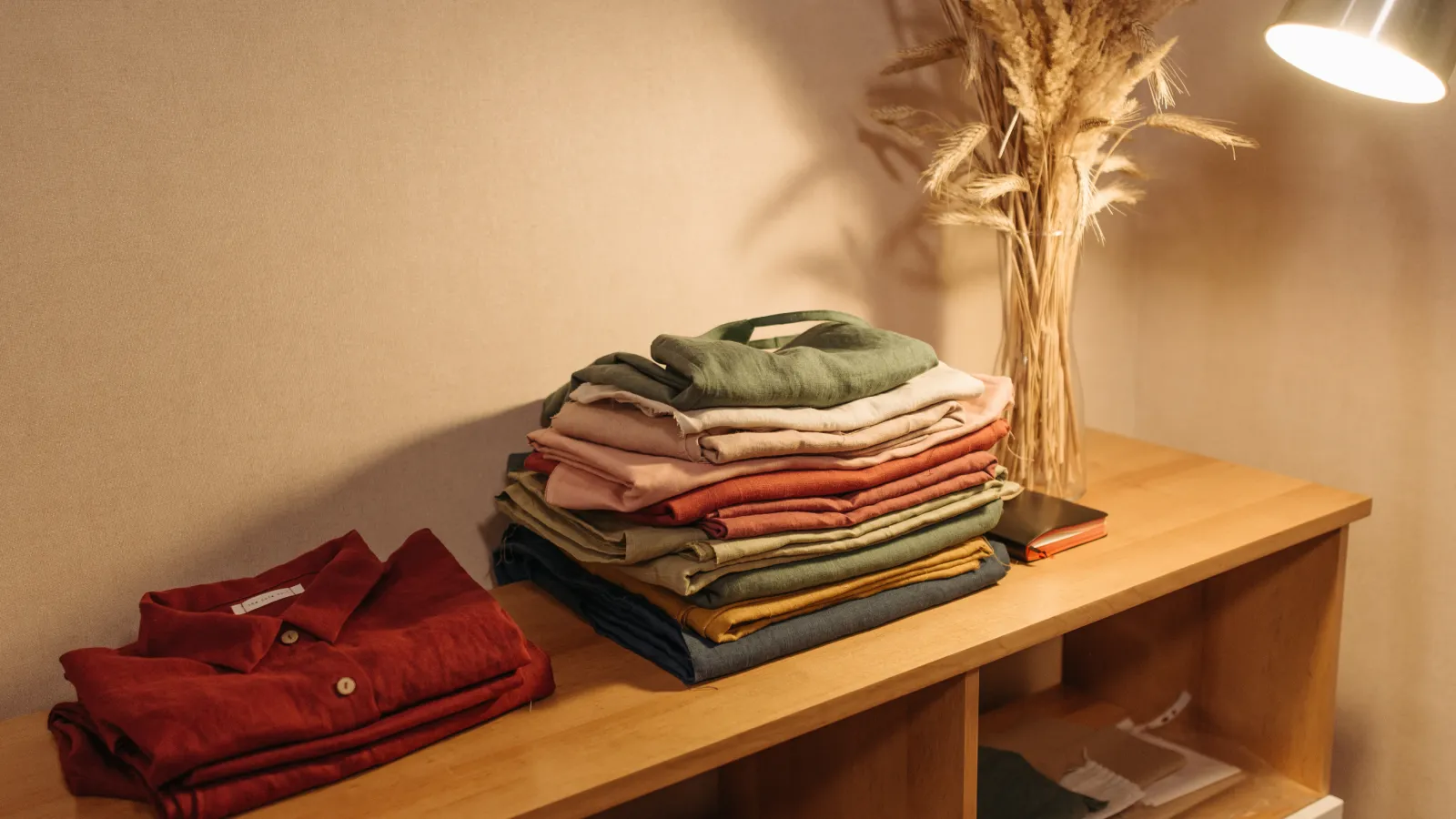 Stack of neatly folded colorful clothes on wooden surface under warm light with dried plants decoration