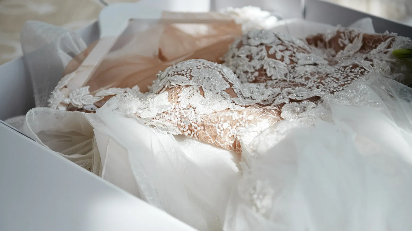 Close-up of a white lace wedding dress with intricate floral embroidery and bead details in soft lighting.