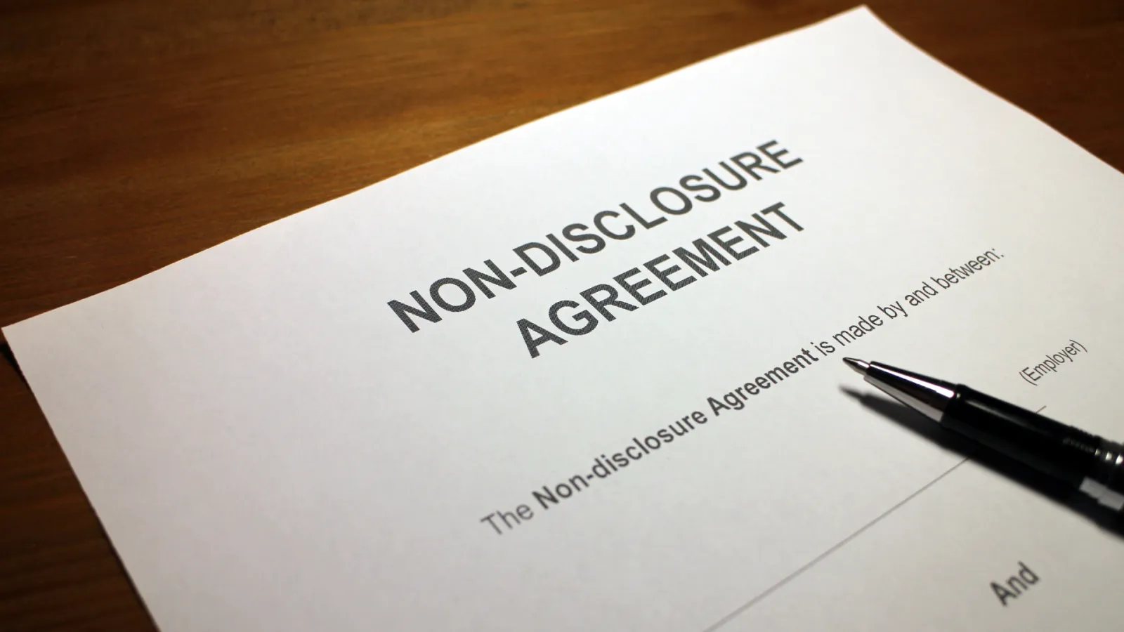 Close-up of a non-disclosure agreement document on a wooden surface with a black pen placed beside it.