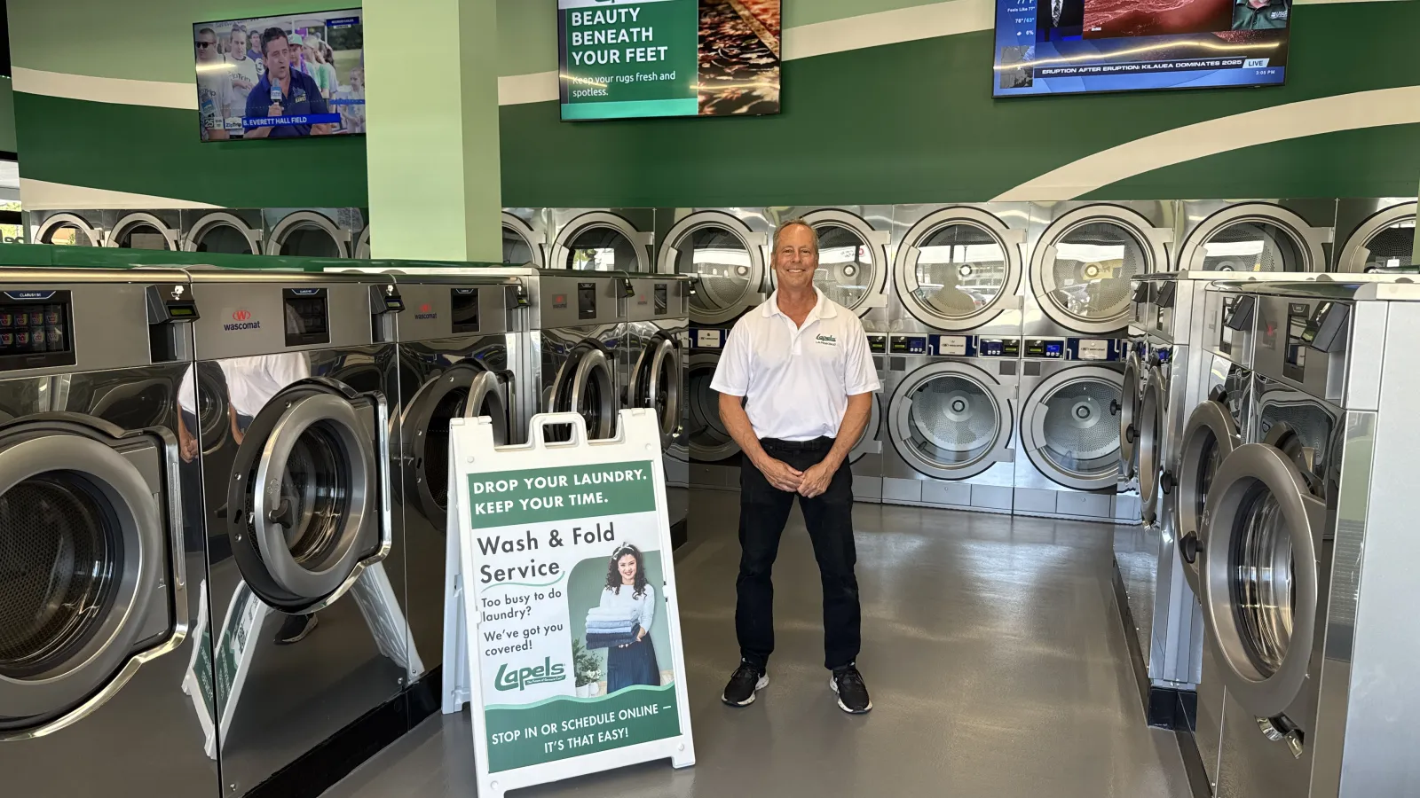Man standing inside laundromat with rows of washing machines and a sign for wash and fold service.