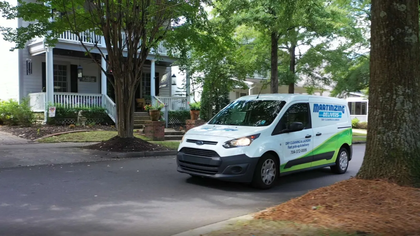 White and green Martinizing delivery van driving on a residential street with trees and houses in the background
