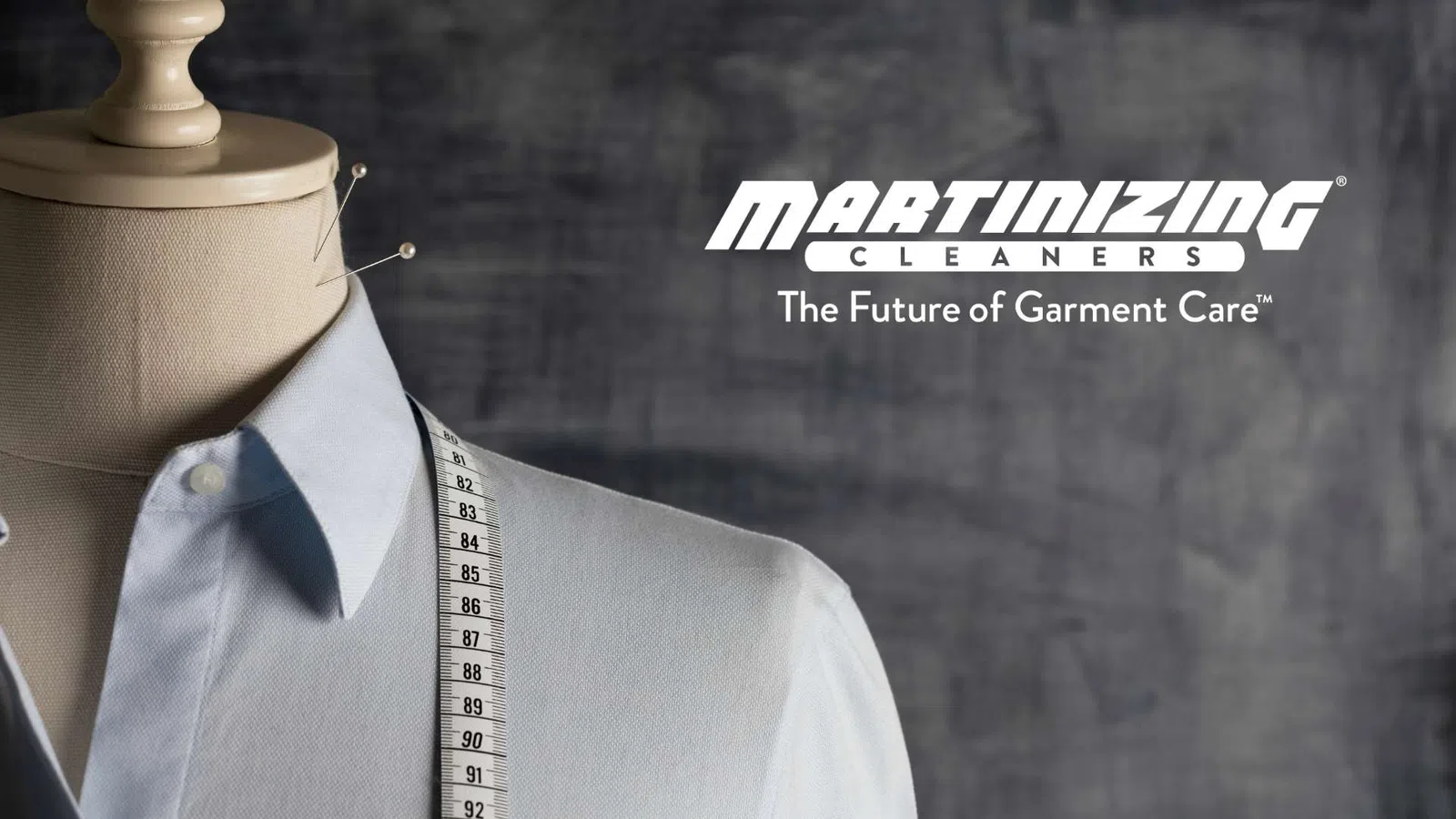 Tailored shirt on mannequin with measuring tape and Martinizing Cleaners logo on textured background.