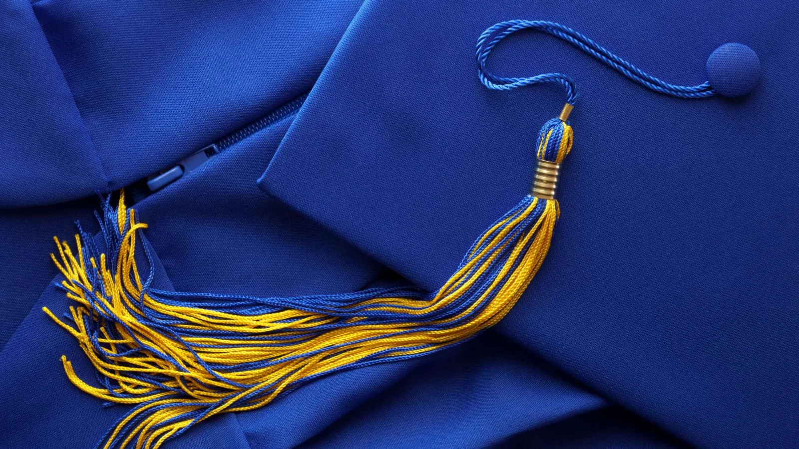 Royal blue graduation cap with a gold and blue tassel resting on matching blue fabric.