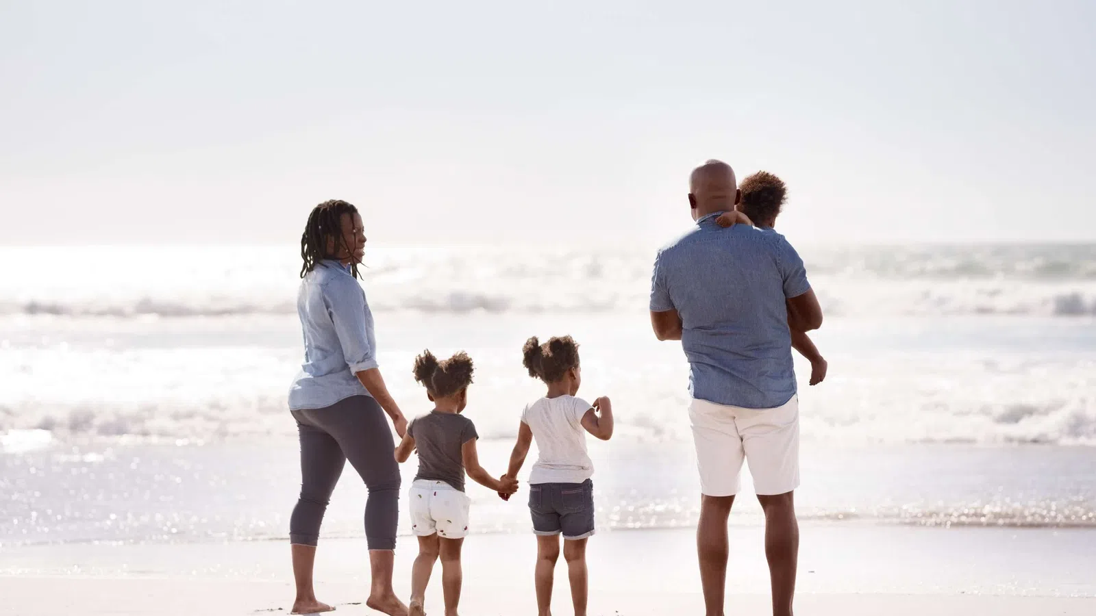 Family of five walking barefoot on the beach near the ocean on a bright sunny day