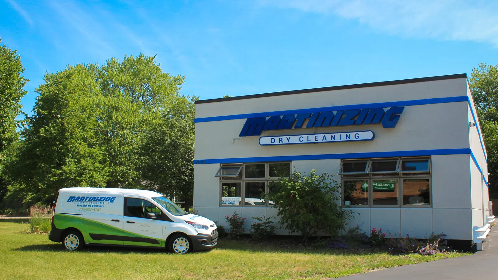 Martinizing Dry Cleaning store with branded service van parked on grass under blue sky with trees in background