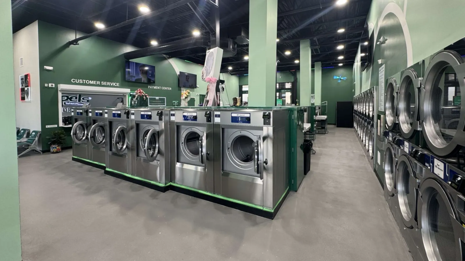 Modern laundromat interior with rows of stainless steel washers and dryers under bright lighting.