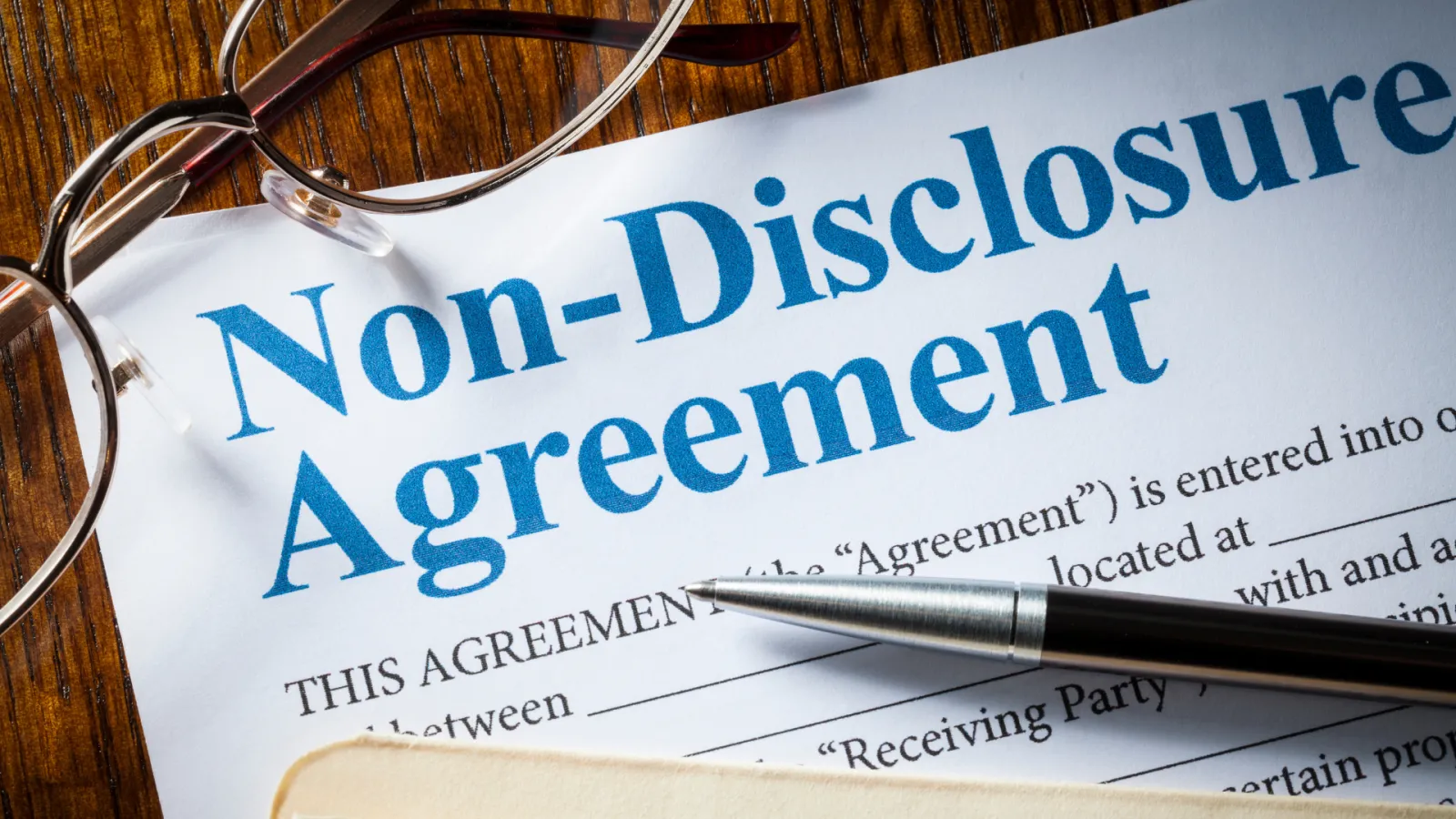 Close-up of Non-Disclosure Agreement document with pen and eyeglasses on wooden table.