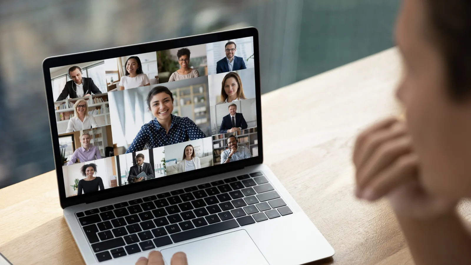 Person participating in a virtual video conference with twelve diverse colleagues on a laptop screen.