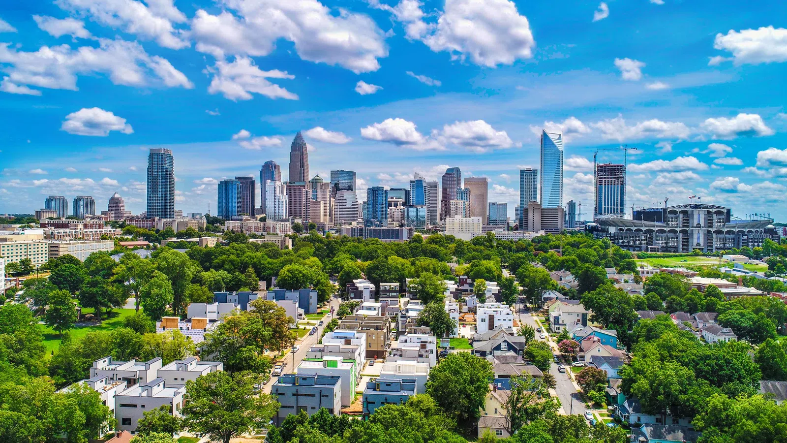 Aerial view of a cityscape featuring mixed-use buildings, greenery, and cloudy sky during daytime.