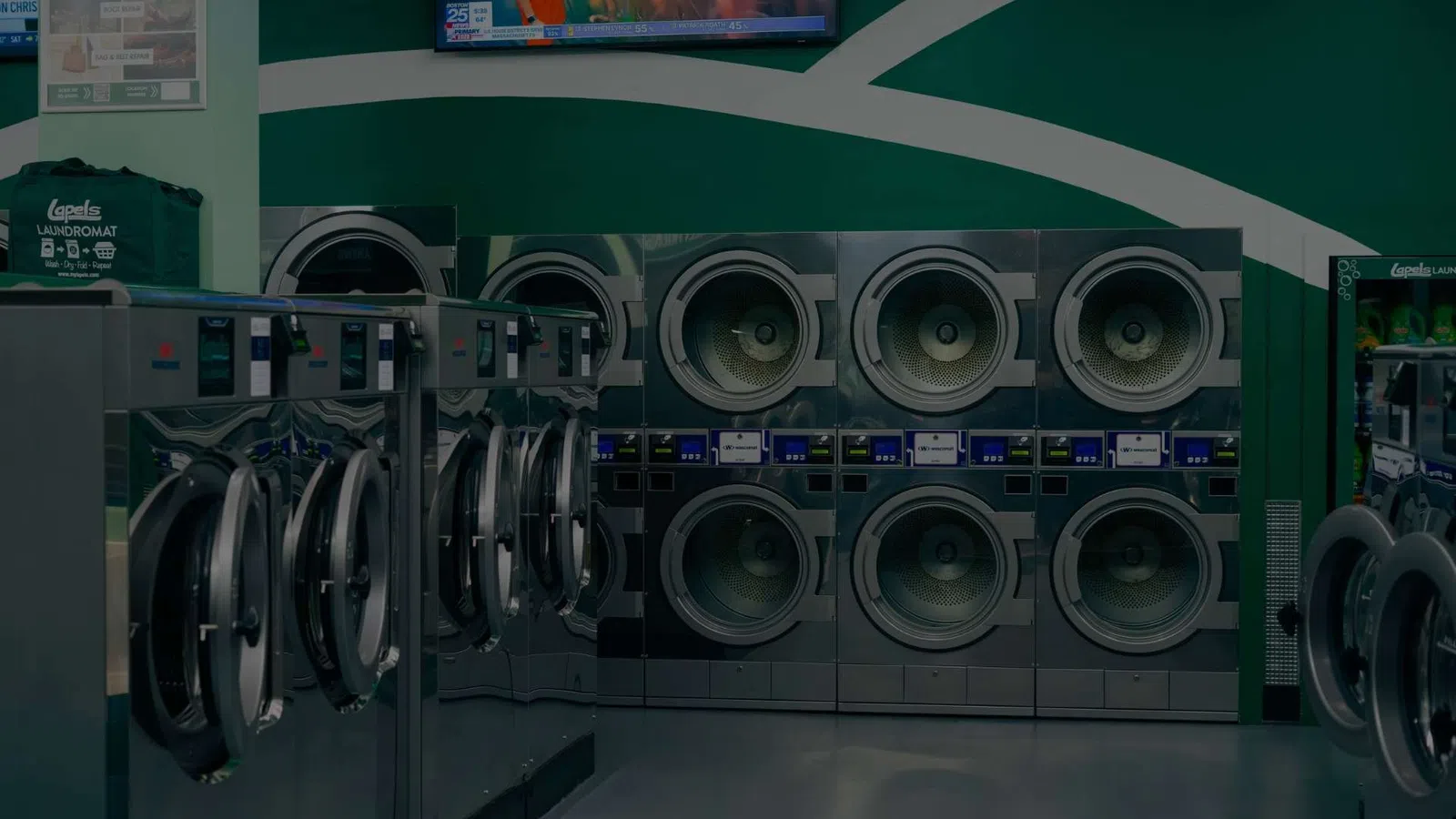 Interior of a laundromat with rows of stainless steel washing machines and a green wall background