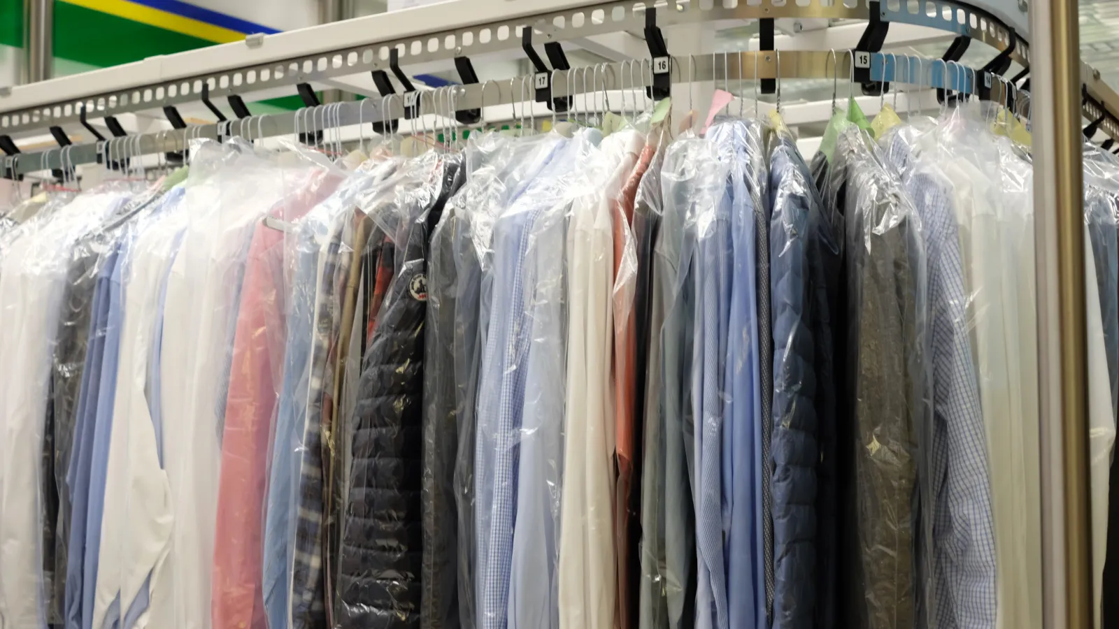 Rack of freshly dry cleaned shirts and jackets covered in plastic hanging in a laundromat or dry cleaner store