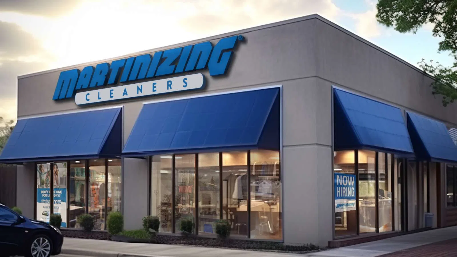 Corner view of Martinizing Cleaners storefront with blue awnings and now hiring sign at sunset.