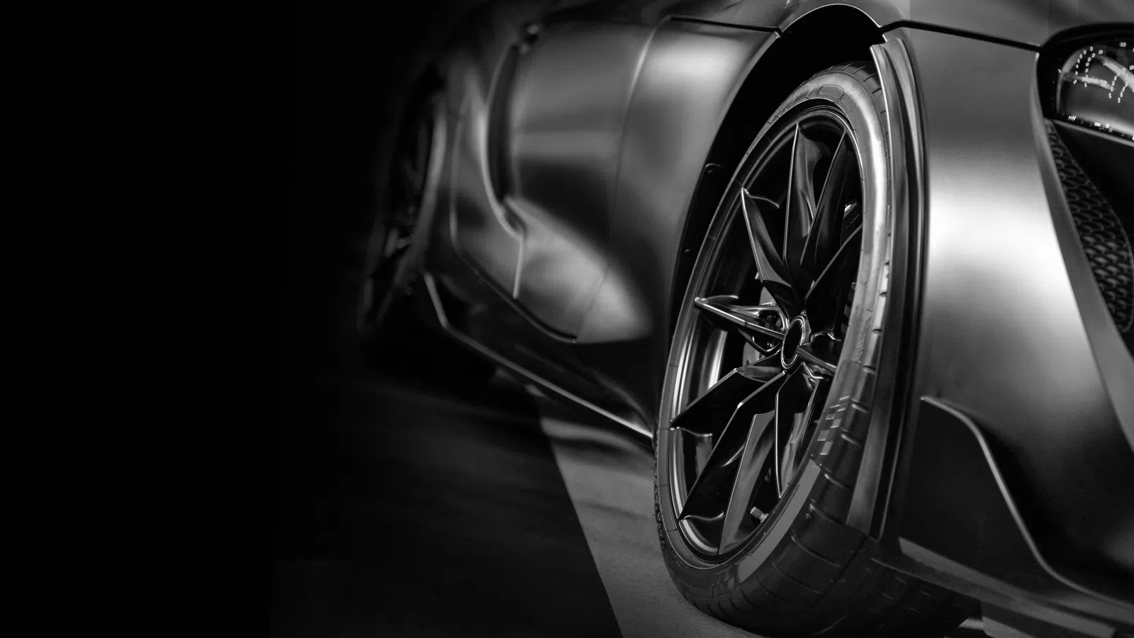 Close-up of sleek black sports car wheel and body showcasing modern design and performance in black and white.