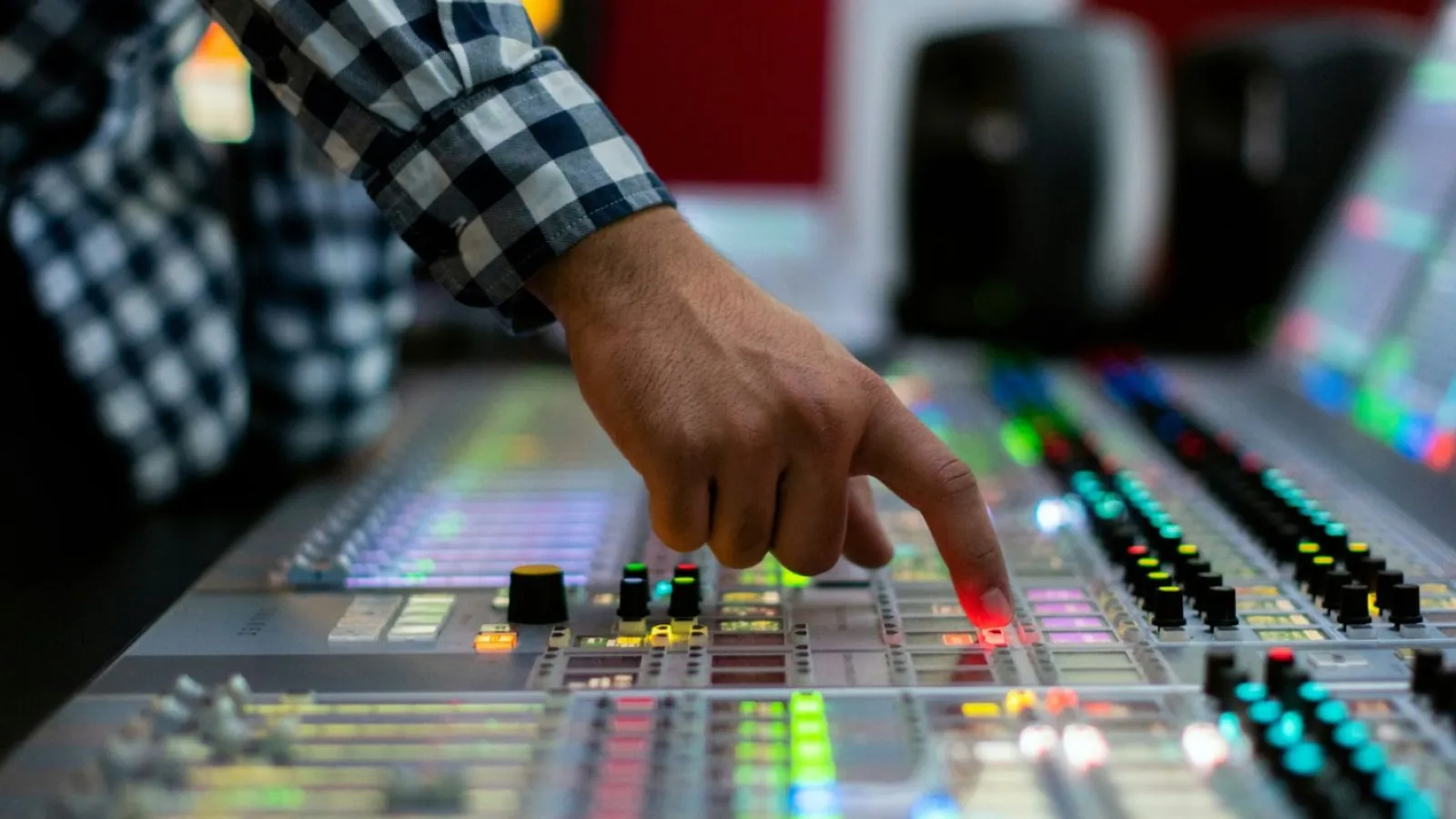 Person adjusting controls on a sound mixing console with colorful lights in a studio environment