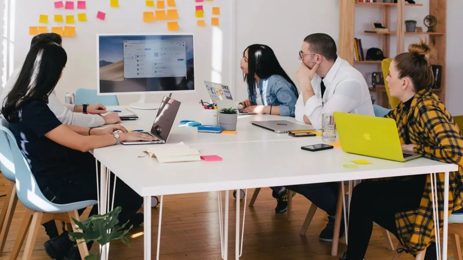 a group of people sitting around a table with laptops