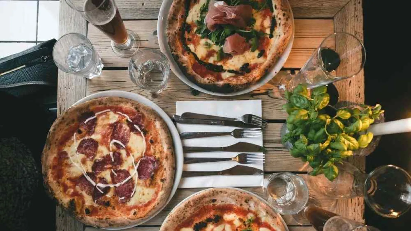 a couple of pizzas on a table with a salad and glasses