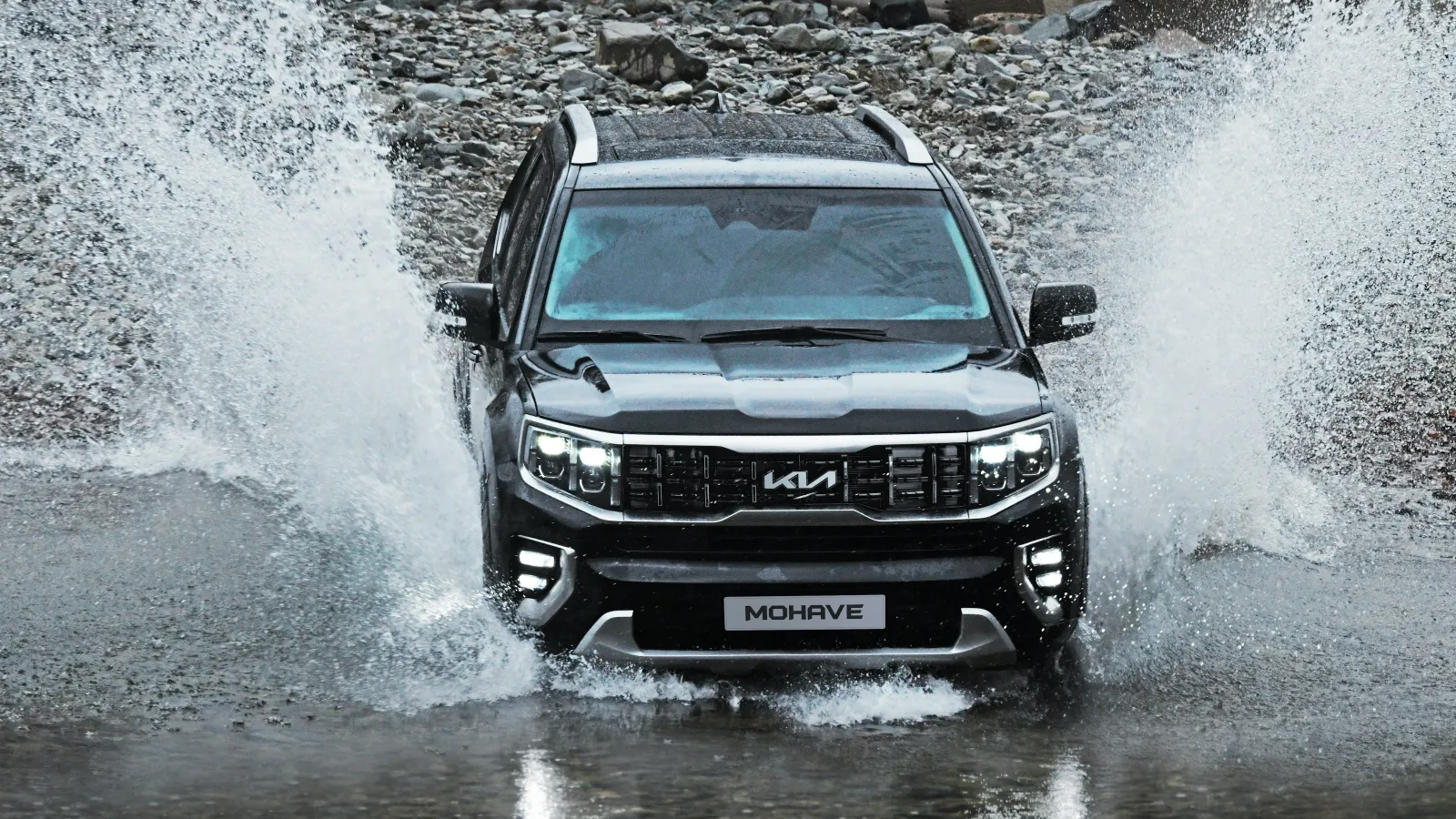 Black Kia Mohave SUV splashing through shallow water on rocky terrain in an outdoor adventure setting.