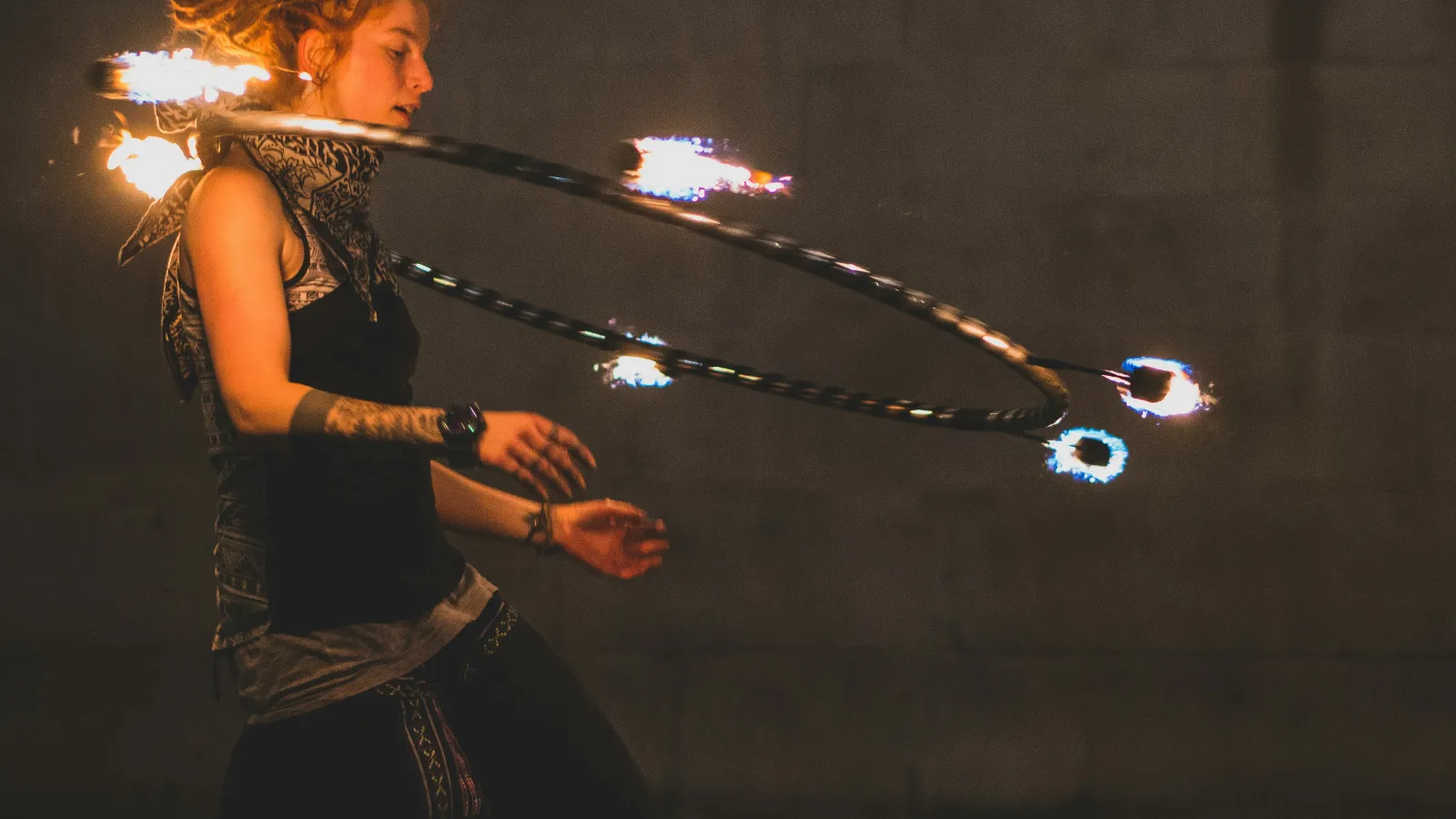 Young woman performing with a flaming hula hoop at night, creating bright fire trails around her body.