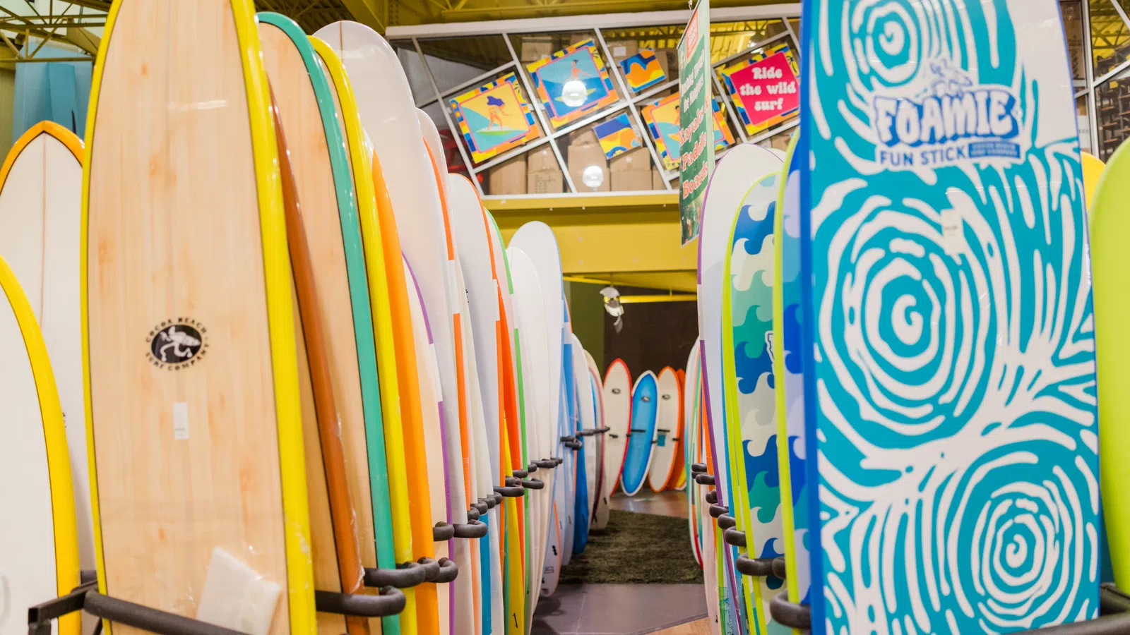 Rows of colorful surfboards displayed upright in a shop with varied designs and vibrant colors.