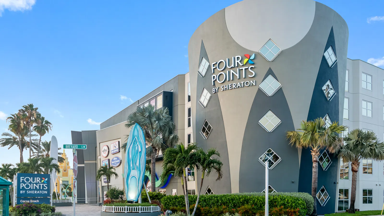 Modern Four Points by Sheraton hotel building with unique curved design and palm trees under a blue sky