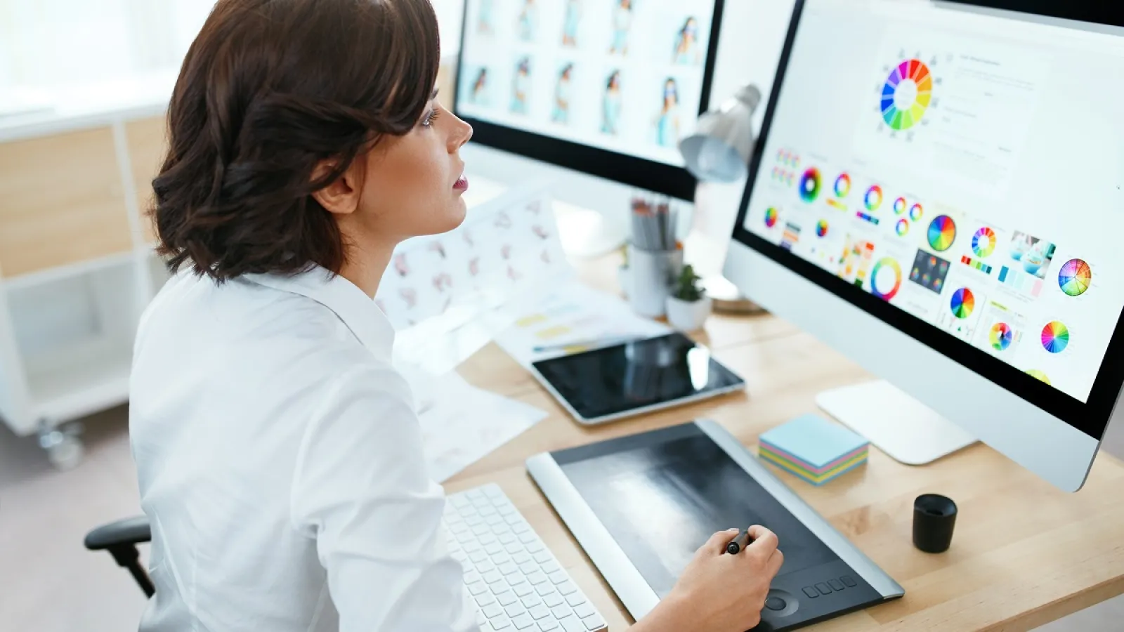 Graphic designer working with color wheels on a computer using a drawing tablet in a bright office.