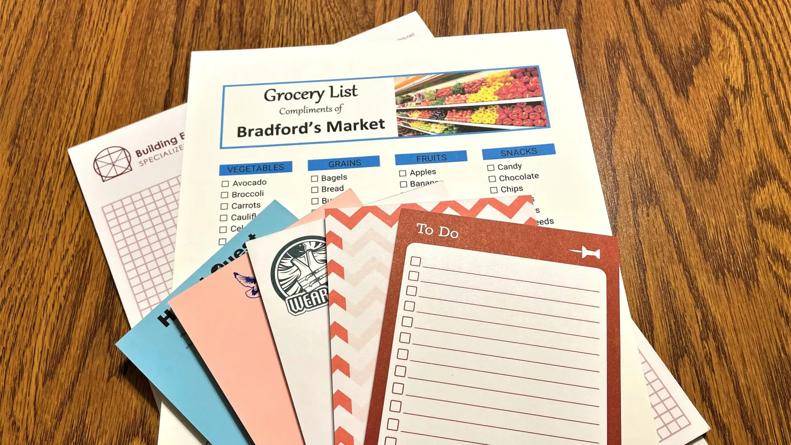 Stack of grocery and to-do lists on a wooden table featuring Bradford's Market checklist and colorful papers