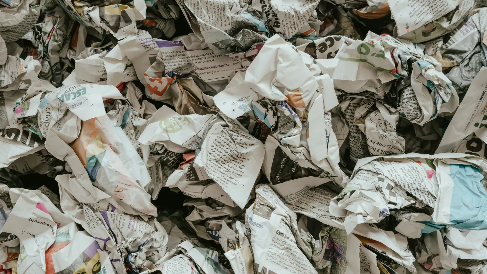 Pile of crumpled newspapers with colorful text and images creating a textured messy background