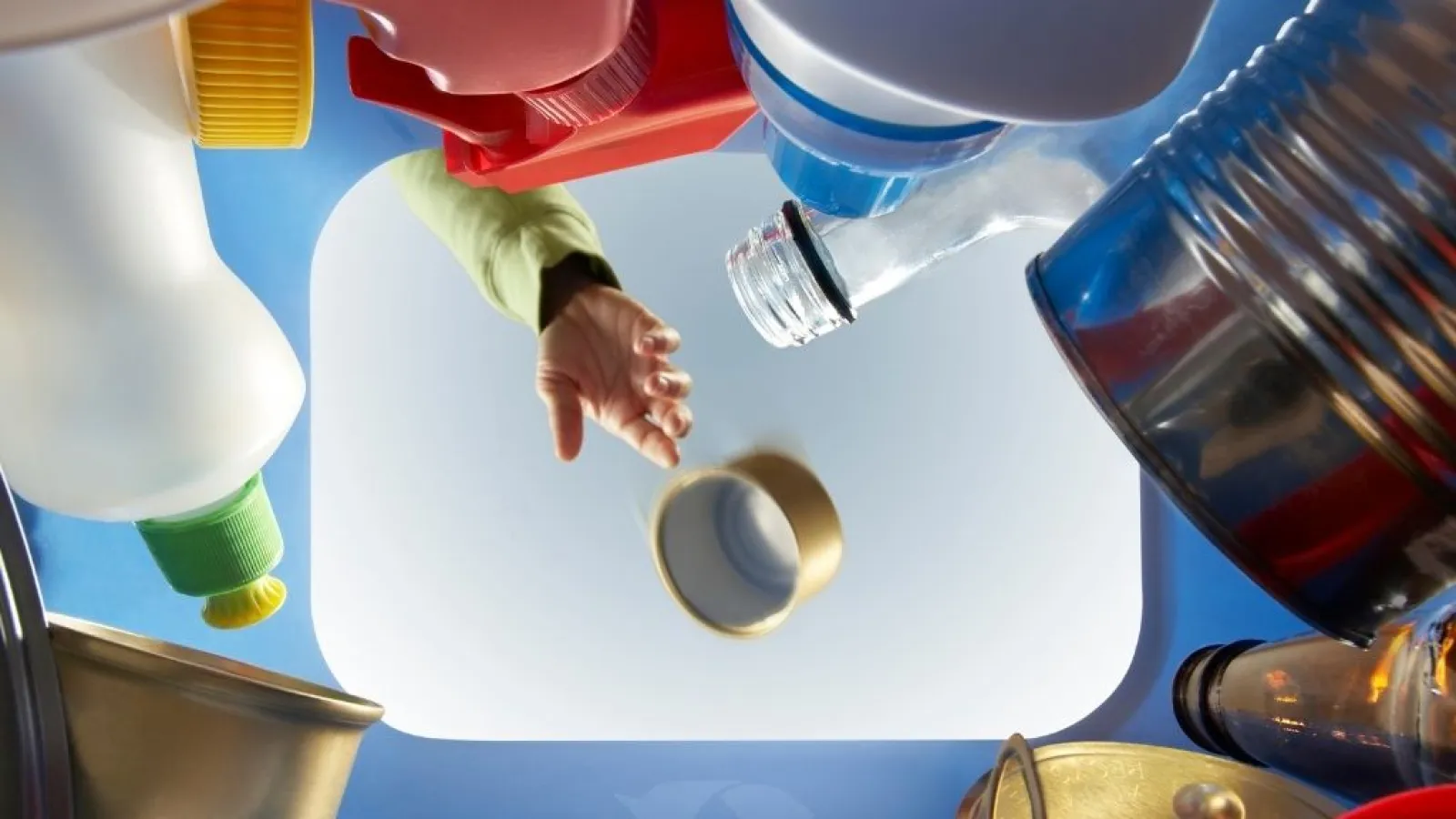 Person throwing recyclable items like bottles and cans into a recycling bin from inside view