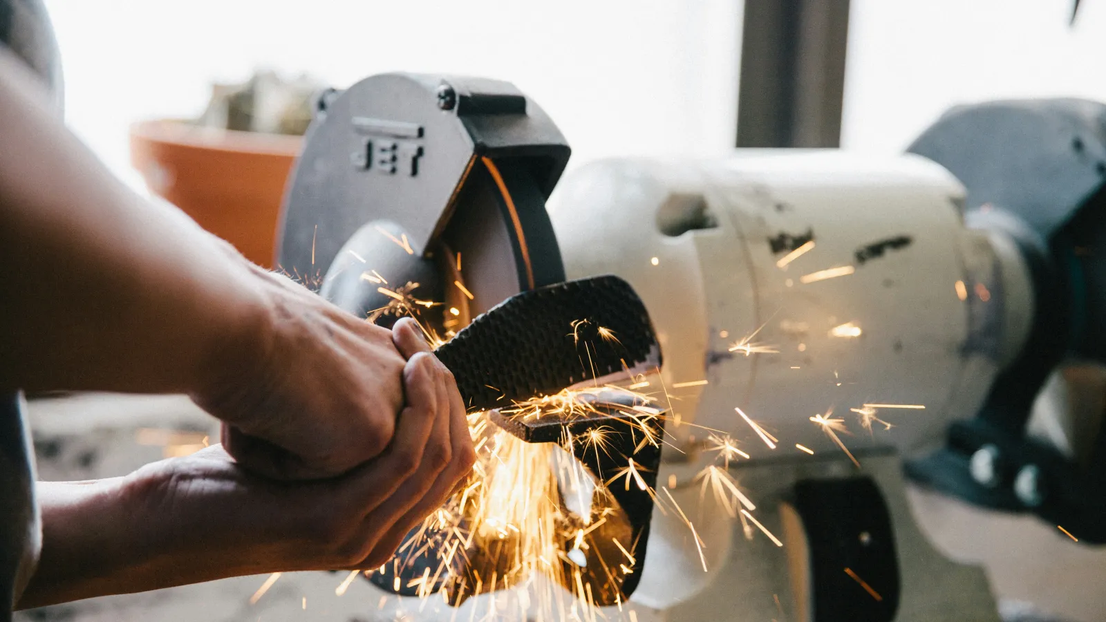 Person sharpening a knife blade with sparks flying from a grinding wheel in a workshop setting