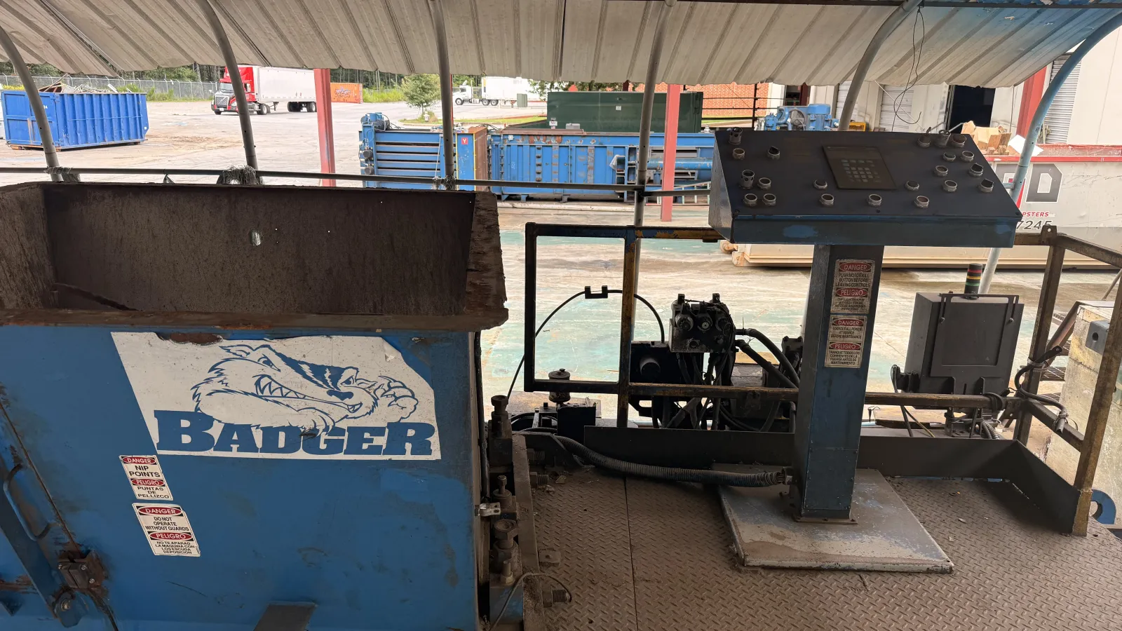 Blue industrial Badger machine with control panel under a metal roof in a work yard.