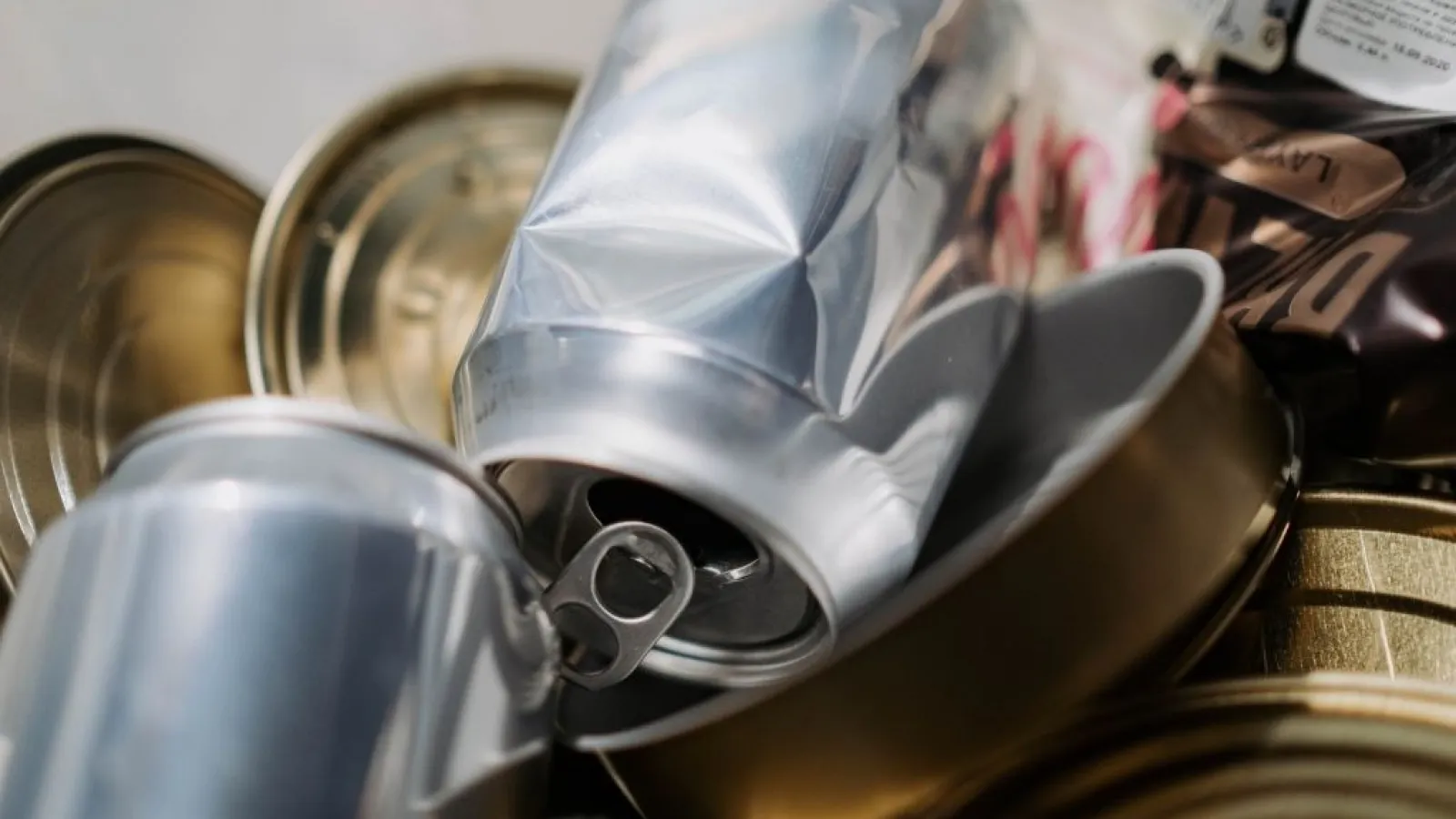 Crushed aluminum cans and metal food tins piled together, symbolizing recycling and waste management.